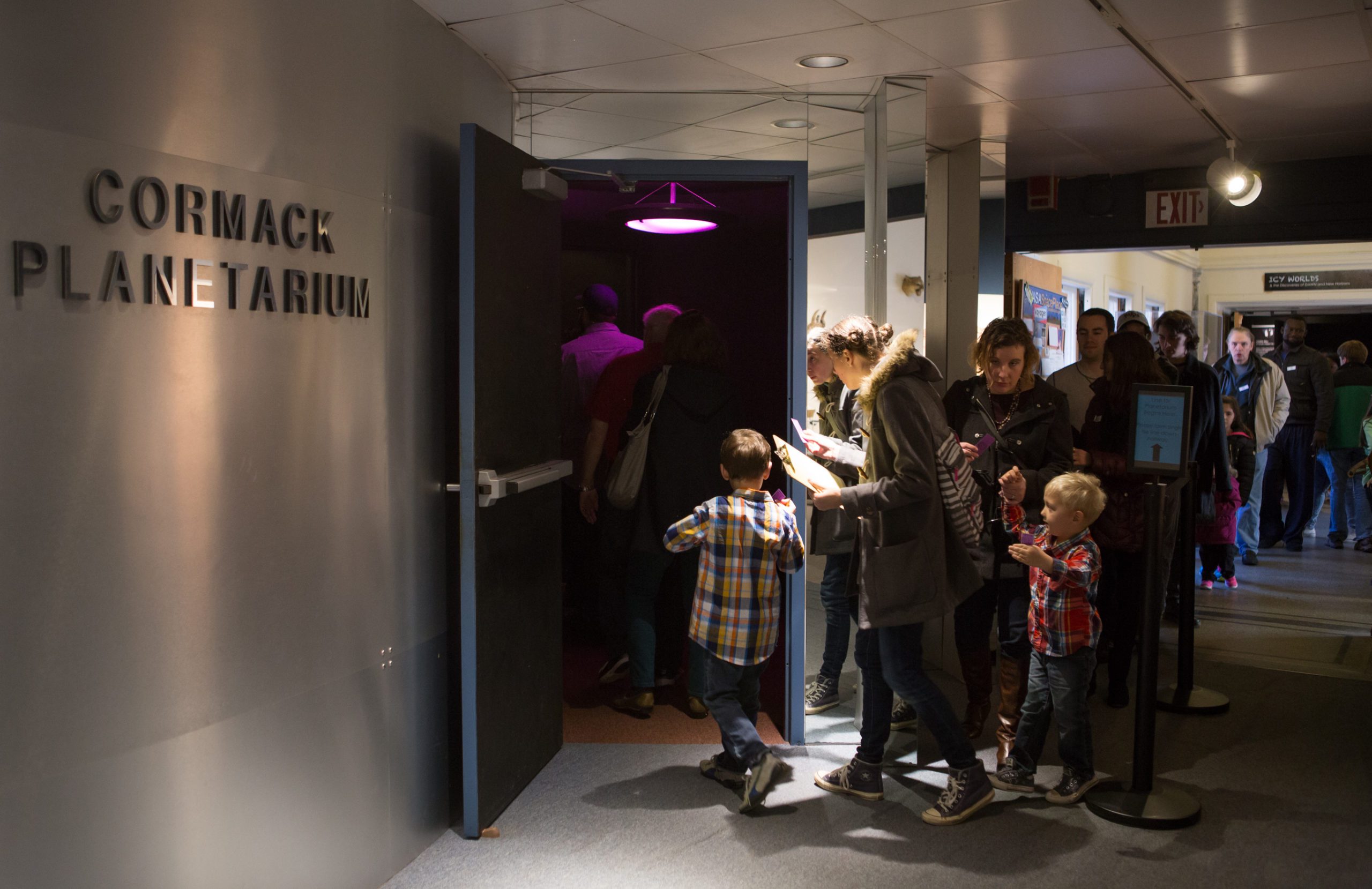 People entering Cormack Planetarium through a door under purple lighting, with a line forming outside.