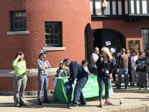 People gather outside a brick building for an Earth Day event at Roger Williams Park. A woman speaks into a microphone.