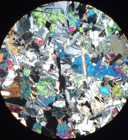 Under a microscope, a kaleidoscope of colorful mineral crystals is visible, showcasing vibrant blues, greens, and reds.