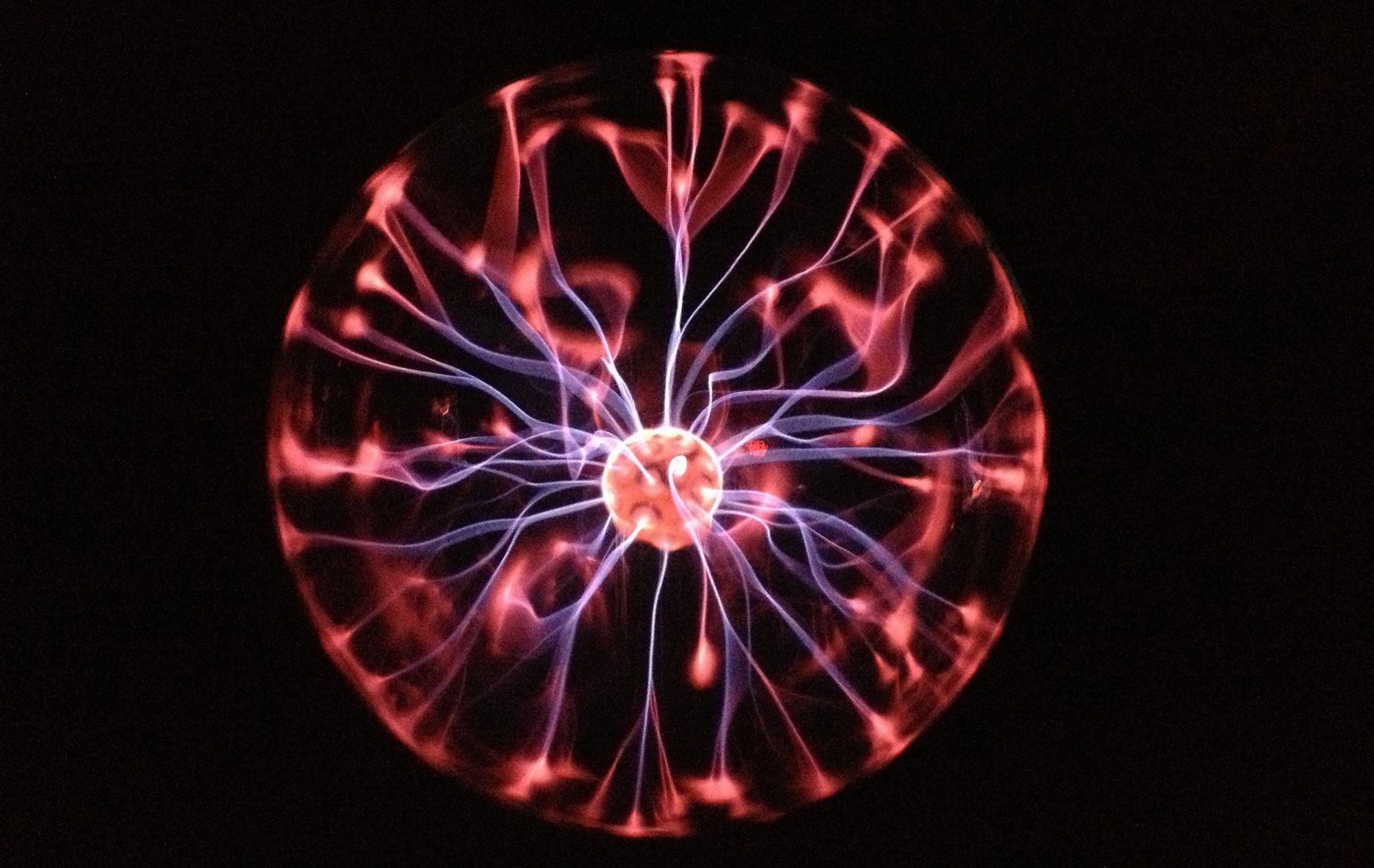 A glowing plasma ball with vibrant pink and purple tendrils emanating from a central sphere against a dark background.