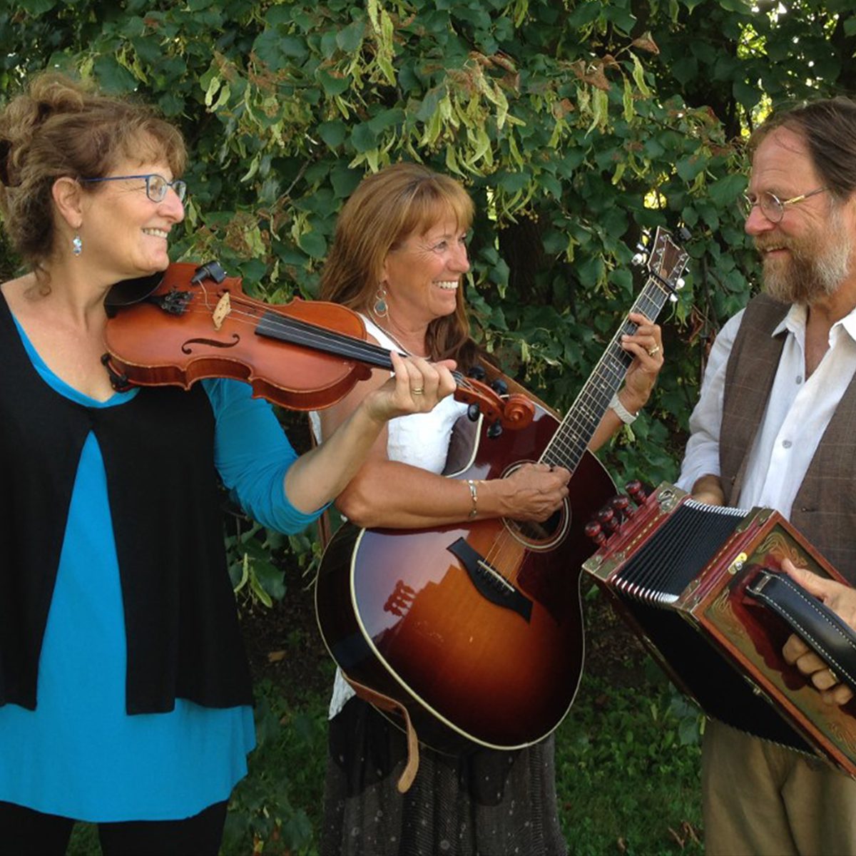Three musicians playing instruments outdoors: one with a violin, another with a guitar, and the third with an accordion, smiling together.