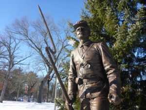 Bronze statue of a Civil War soldier with a bayonet, set against a backdrop of trees and a clear blue sky.