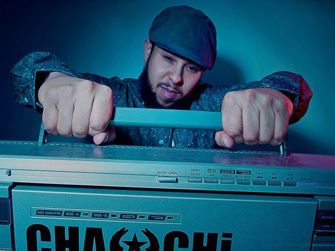 Chachi Carvalho holds a boombox handle, wearing a cap and patterned shirt. The boombox displays "CHA CHI" prominently.