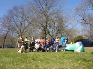 A group of people poses outdoors on a sunny day in front of a table with a "Roger Williams Park" banner.