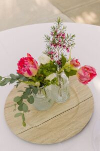 Elegant flower arrangement with pink and white roses, greenery, and small pink blooms in glass vases on a wooden tray.