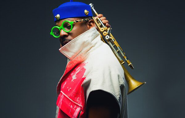 A man with a trumpet rests on his shoulder, wearing a colorful outfit and round green glasses.