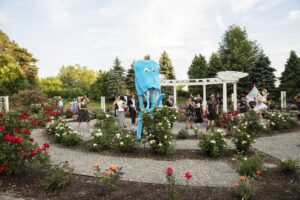 A blue octopus costume stands among people in a rose garden, with musicians and attendees enjoying the event.